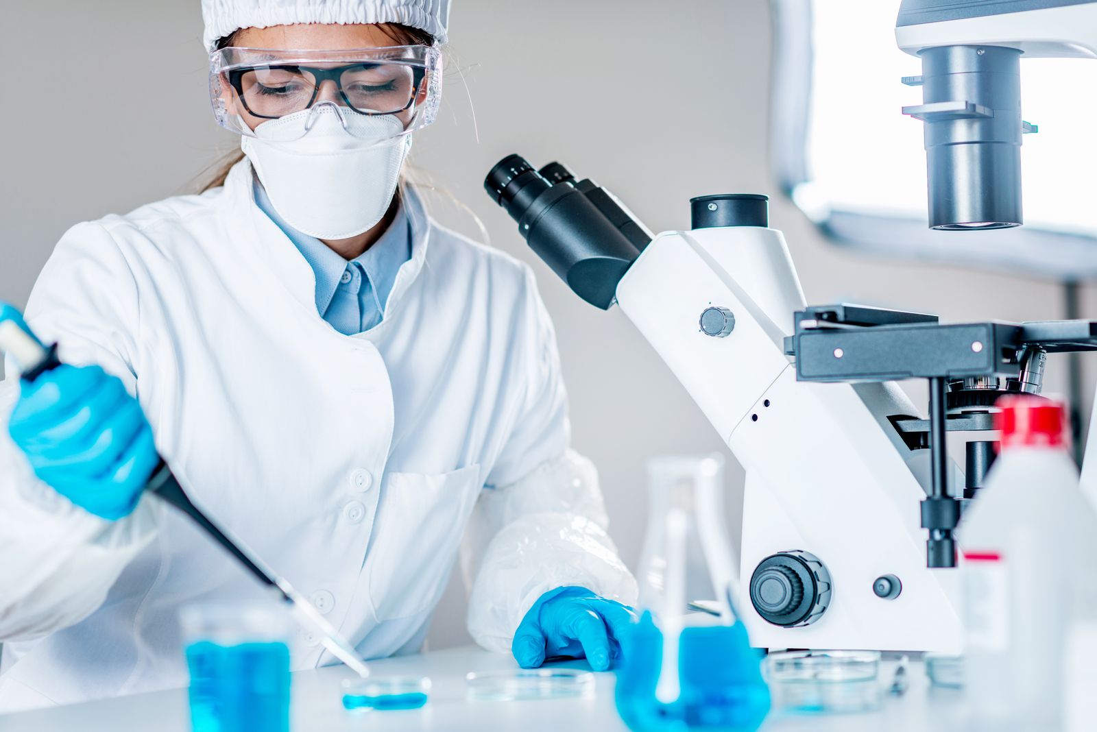 Laboratory scientist in PPE pipetting a sample beside a microscope